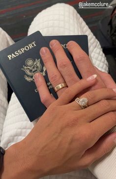 a person holding a passport and two wedding rings on their fingers, with the other hand in front of them