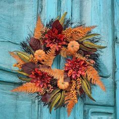 a wreath made out of fake leaves and pumpkins on a blue door with autumn colors