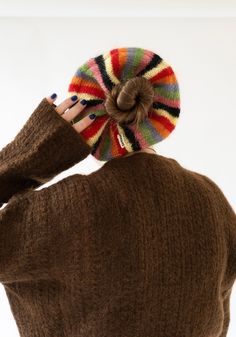 a woman with her hand on the back of her head wearing a brown sweater and multi - colored knitted hat