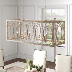 a chandelier hanging over a dining room table with chairs and flowers on it