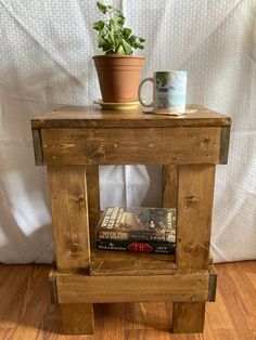 a small wooden end table with a plant on top and some books in front of it