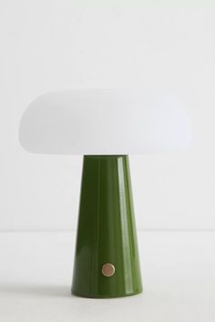 a green table lamp with a white shade on it's top and a gold dot at the base