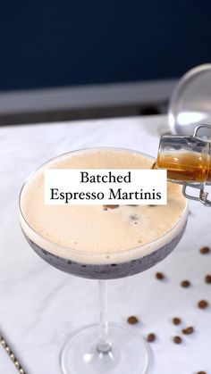 a glass filled with a drink sitting on top of a table next to coffee beans