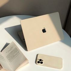 an apple laptop computer sitting on top of a table next to a book and phone