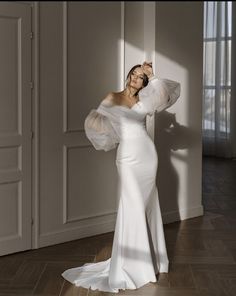 a woman in a white dress posing for the camera with her arms behind her head