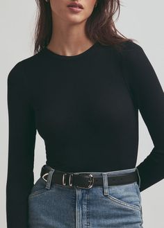 a woman wearing a black top and jeans with her hands on her hips, looking at the camera