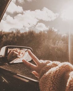 a person's hand on the side mirror of a car with clouds in the background