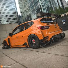 an orange sports car parked in front of some tall buildings