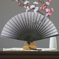 a white and black fan sitting on top of a table next to a vase with pink flowers