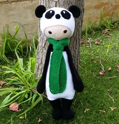 a knitted panda bear wearing a green scarf next to a tree in the grass