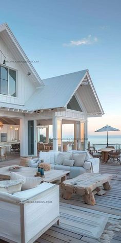 an outdoor living area with couches, tables and chairs on a wooden deck overlooking the ocean