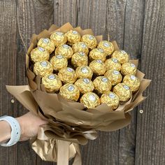 a person holding a bouquet of chocolates in front of a wooden fence with brown paper wrapped around it