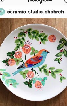 a plate with a bird painted on it sitting on a wooden table next to a phone