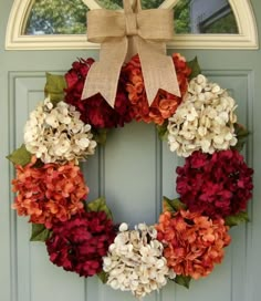 a wreath with red and white flowers hanging on the front door to welcome someone in their home