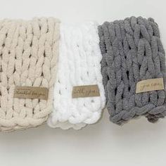 three different colored knitted items with tags on the handles and sides, one is white, one is gray