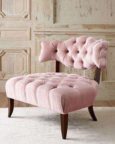 a pink velvet chair with wooden legs and buttons on the back, in front of a wall