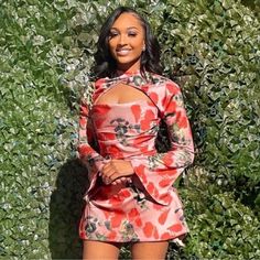 a woman standing in front of a bush wearing a red floral dress and matching heels