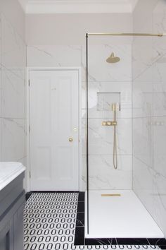 a white bathroom with black and white flooring, gold fixtures and a walk in shower