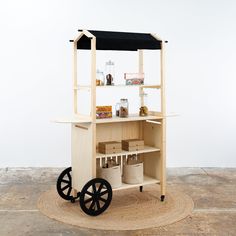 a wooden cart with wheels and shelves on top of it, in front of a white wall