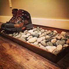 a pair of hiking boots sitting on top of rocks in a wooden tray filled with water