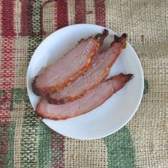 two slices of bacon on a white plate sitting on a tablecloth covered surface with red and green stripes