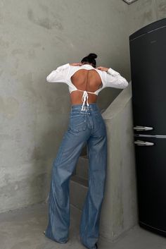 a woman with her back to the camera, leaning against a wall and looking down