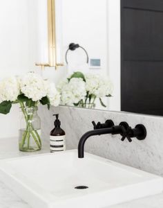 a white sink sitting under a bathroom mirror next to a vase with flowers in it