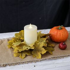 a white candle sitting on top of a table next to some leaves and an apple