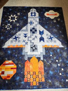 a quilted wall hanging with an image of a space shuttle in the sky on it