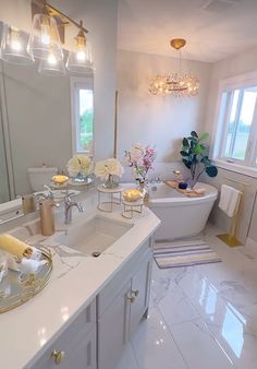 a white bathroom with two sinks and a bathtub in the middle, along with a chandelier