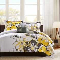 a bed with yellow and gray flowers on the comforter in front of a window