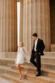 a man and woman holding hands while walking up some steps