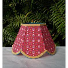 a pink lamp shade sitting on top of a table next to green plants and trees