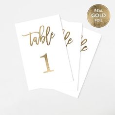 three gold foil table numbers on white paper with the number one printed in gold ink