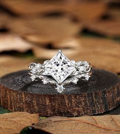 an engagement ring sitting on top of a piece of wood with leaves around the band