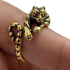 a close up of a person's hand holding a gold ring with a tiger on it