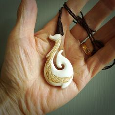 a person holding a white and gold pendant in their hand with brown cords around it