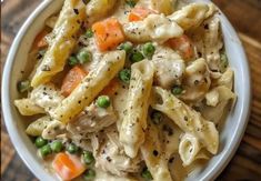 a white bowl filled with pasta and vegetables on top of a wooden table next to a fork