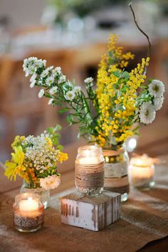 two vases filled with yellow and white flowers sitting on top of a wooden table