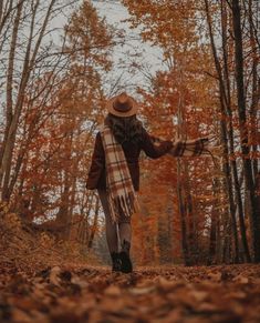 a woman wearing a hat and scarf walks through the woods in autumn with her arms outstretched