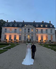 a bride and groom walking towards a large mansion at night with lights on the windows