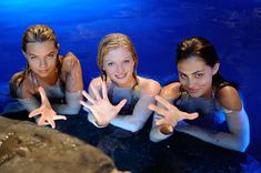 three girls are in the water with their hands up