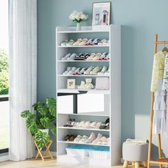 a white shelf filled with baby shoes next to a window and potted plant in front of it