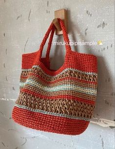 an orange crocheted bag hanging from a hook on a white wooden wall,