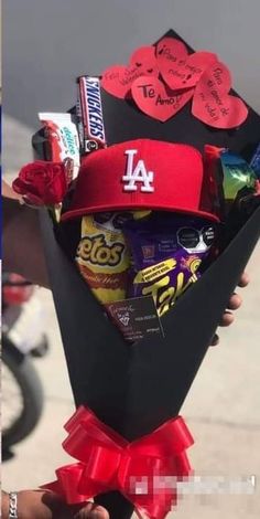 a man holding a bouquet of candy and candies in his left hand while wearing a los angeles hat