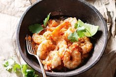 a bowl filled with shrimp and cilantro on top of a table next to a fork