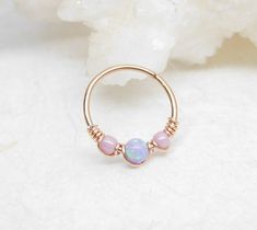 a gold ring with pink and white opal beads sitting on top of a rock