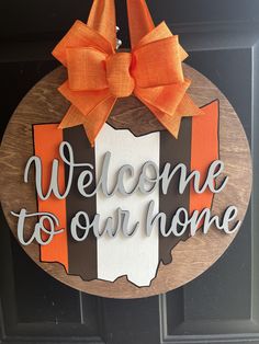 a welcome to our home sign hanging on a door with an orange and white bow