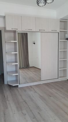 an empty room with white walls and wooden flooring, open doors to the closet