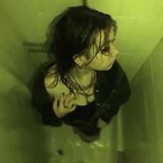 a woman in black shirt sitting on top of a urinal next to a toilet